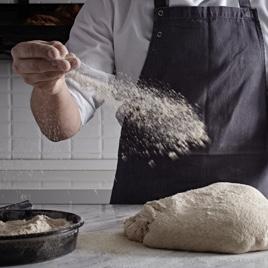 Man with white shirt and black apron dusting flour over dough